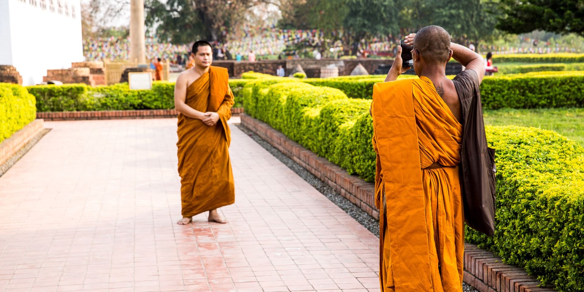 Monks wearing gold robes, one taking a photo of the other in Lumbini, Nepal